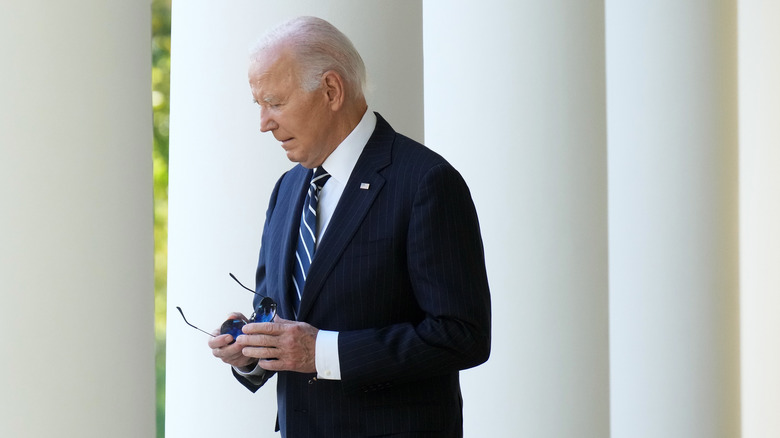 Joe Biden walking outside of White House holding sunglasses