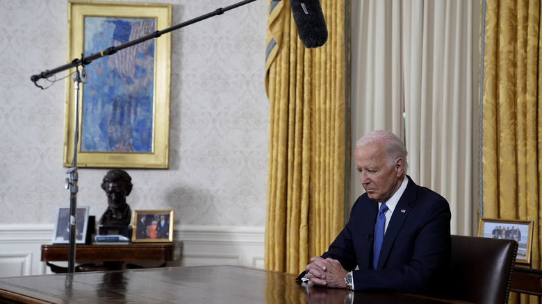 President Biden behind desk looking down with boom mike