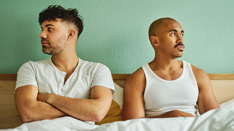 Couple sits tense in bed, arms crossed