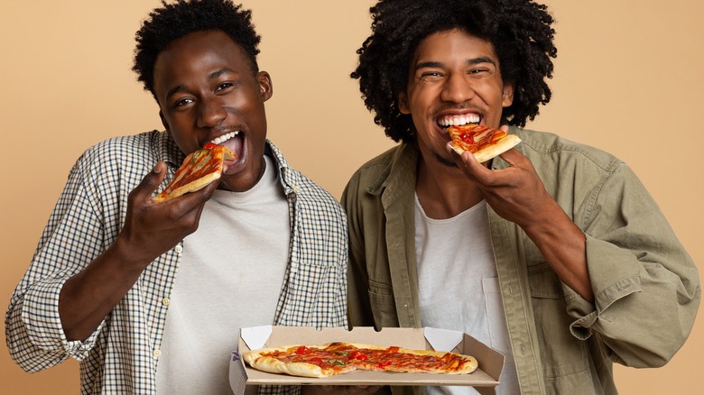 two men smiling and eating pizza