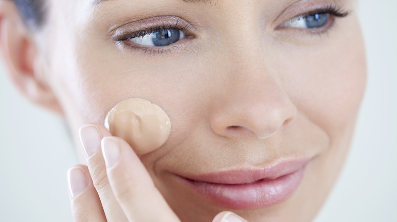 Woman applying foundation to her cheek