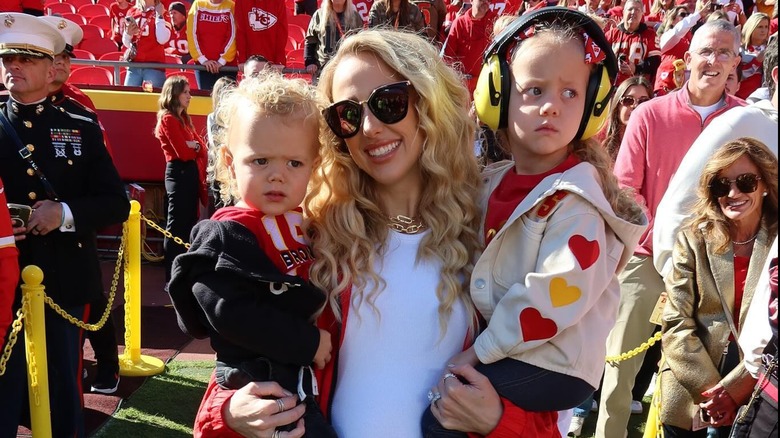 Brittany Mahomes with curly hair smiling while holding her kids