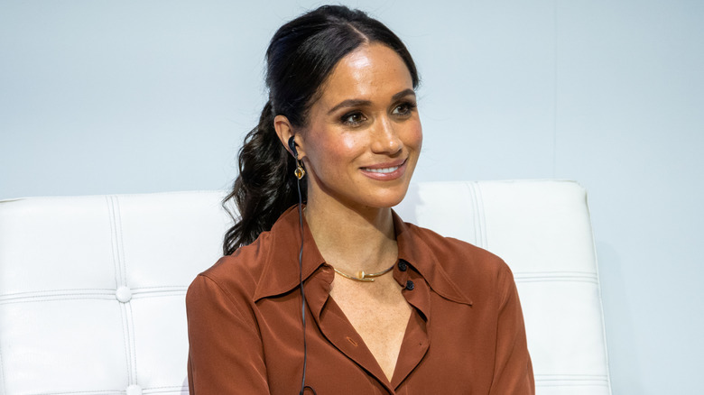 Meghan Markle in a brown button up shirt and ponytail