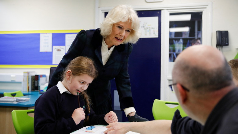 Camilla, Duchess of Cornwall interacts with a pupil and a member of staff during a visit to the Roundhill Primary School on February 8, 2022 in Bath, England