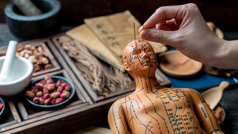 hand placing needles in acupuncture doll