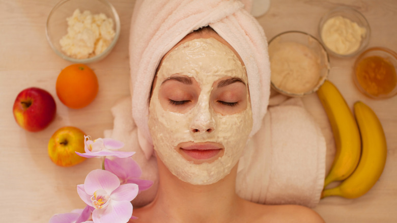 Woman with face mask surrounded by fruit including bananas