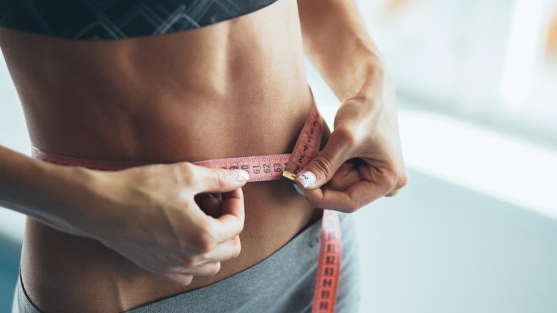 woman with visible abs using tape measure healthy unhealthy