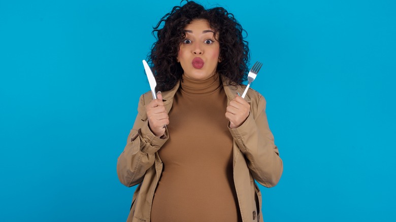 pregnant woman holding up a fork and knife