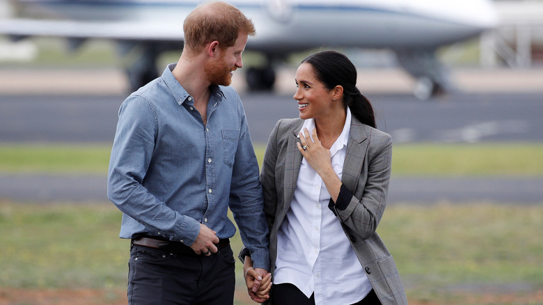 Prince Harry and Meghan Markle smiling at each other at an event. 