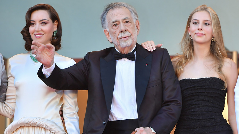 Francis Ford Coppola waving to an audience with Aubrey Plaza and Romy Mars at the Cannes Film Festival