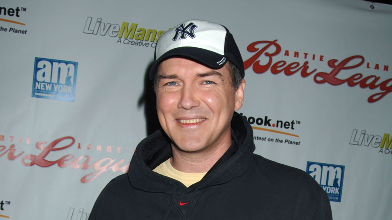 Norm Macdonald wearing a baseball cap and smiling