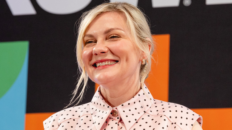 Kirsten Dunst smiling in a pink polka-dotted outfit