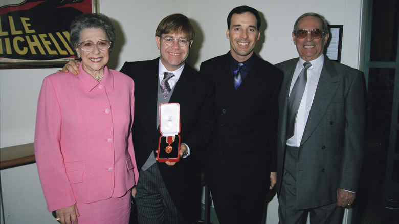 Elton John poses for a photo with his parents and partner, David Furnish after receiving his knighthood