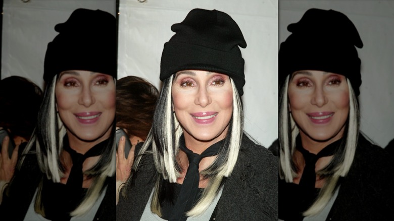 Cher smiling while wearing a black and blond wig