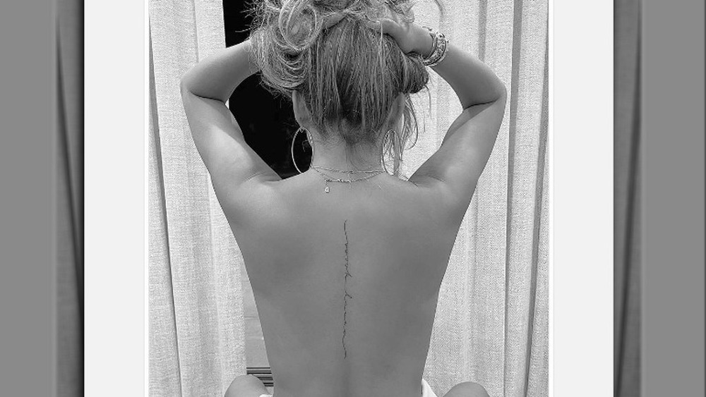 Chrissy Teigen holding up hair to show off back tattoo