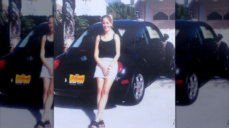 Christina Haack posing as a teenager in a mini skirt by a black car