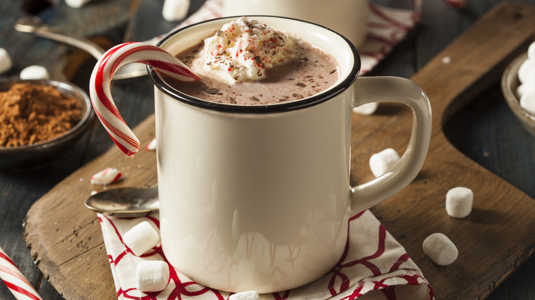 A mug of hot chocolate with a candy cane and whipped cream for garnish