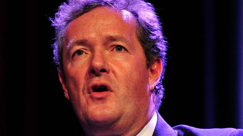 Piers Morgan holds a hand up onstage