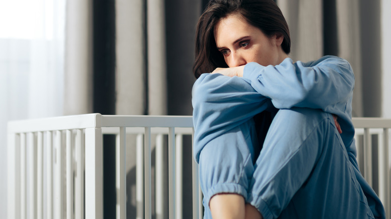 Woman sitting on bed next to baby crib