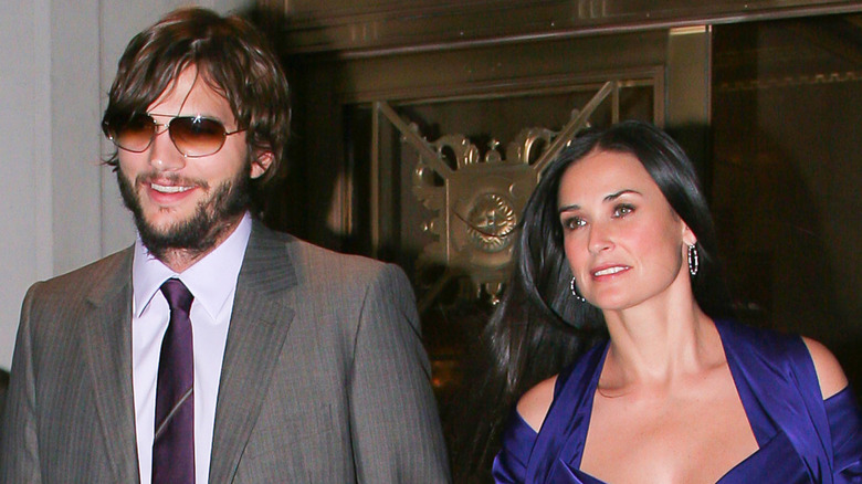 Ashton Kutcher smiling in sunglasses walking next to Demi Moore in blue dress