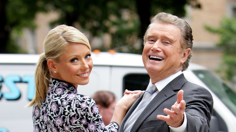 Kelly Ripa placing hand on Regis Philbin's shoulder outdoors