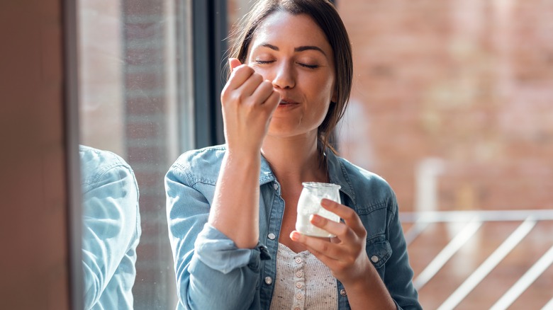 Woman eating yogurt in front of a window