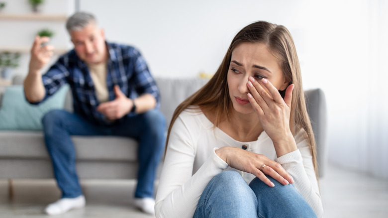 couple arguing while a woman wipes a tear away