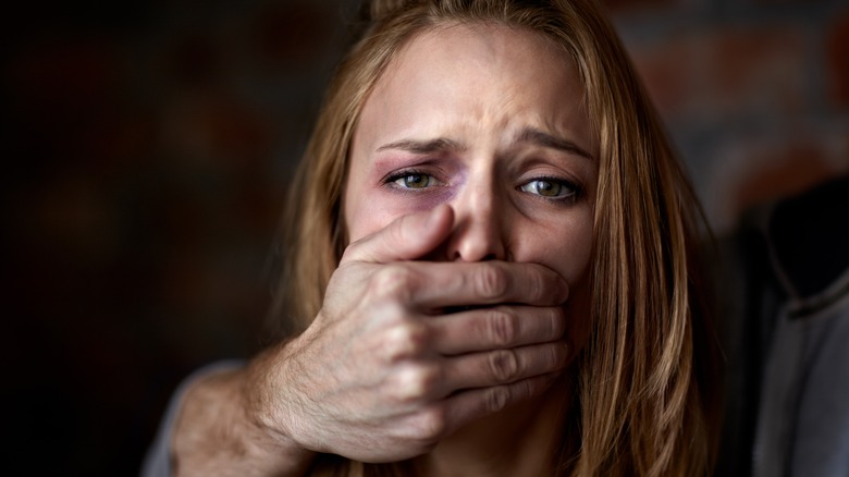 woman being silenced by her abuser with his hand over her mouth