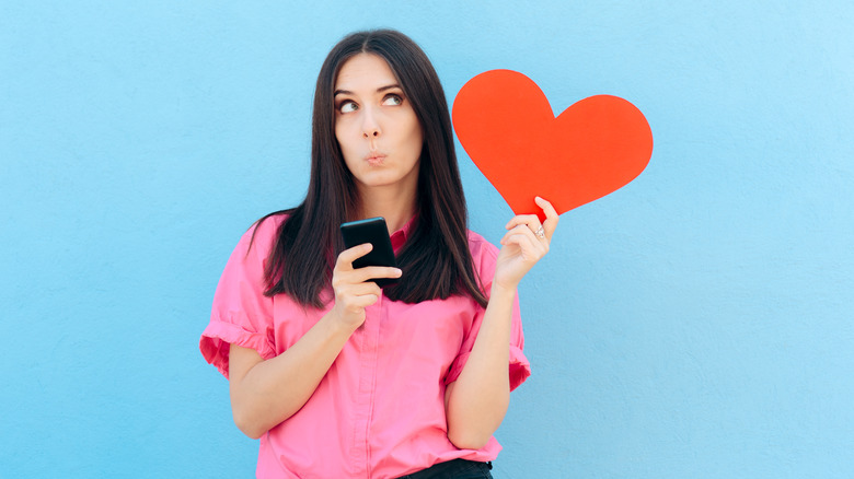 Woman holding a paper heart in one hand and her phone in the other