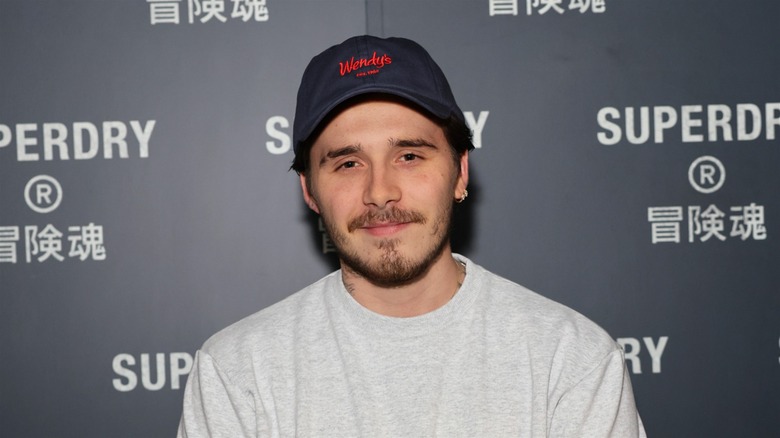 Brooklyn Beckham smiling on a Superdry step-and-repeat in a Wendys hat