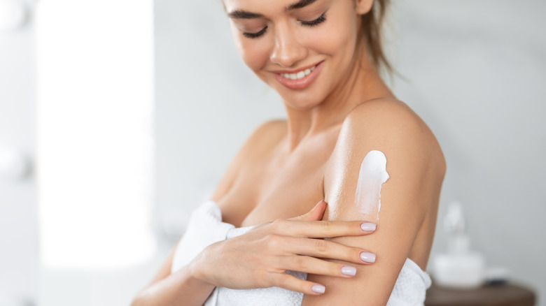 A woman applying lotion on her shoulders