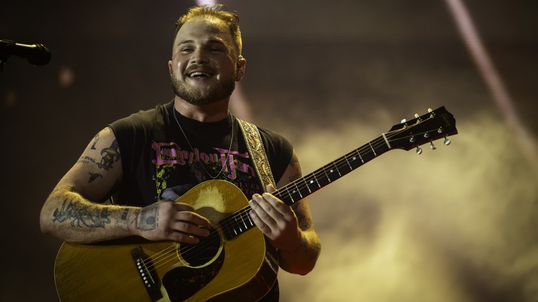 Zach Bryan smiling and performing on stage