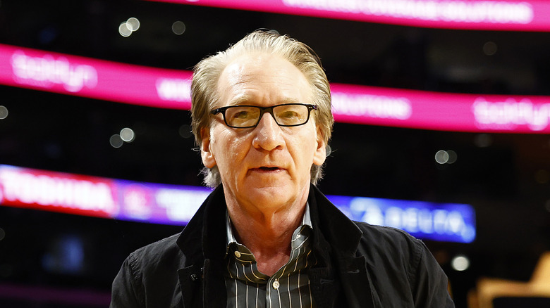 Bill Maher wearing glasses and a dark coat