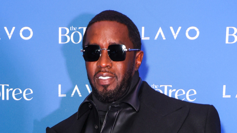 Sean "Diddy" Combs smiles while standing against a blue banner