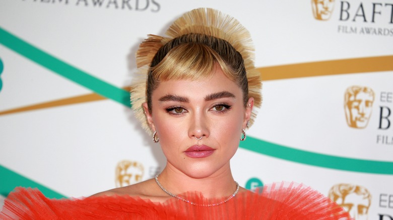 Florence Pugh posing at a BAFTA event in an orange dress with spiky hair