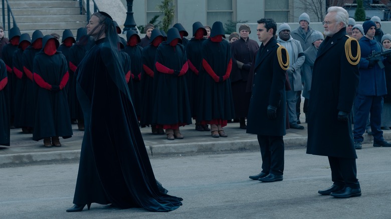 Serena (Yvonne Strahovski), Nick (Max Minghella) and Commander Lawrence (Bradley Whitford) walking in front of handmaids