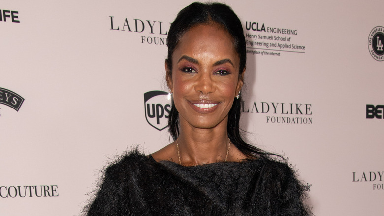 Kim Porter smiles while posing in a black outfit and simple accessories