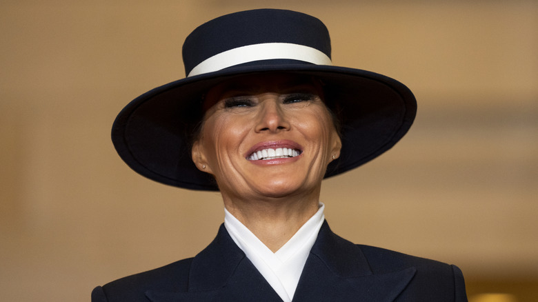 Melania Trump smiling widely in a wide-brimmed hat