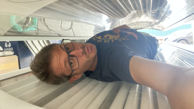 Alex Lehmann posing in the tanning bed time machine from Meet Cute