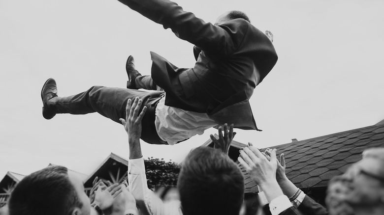 Wedding guests tossing groom up 