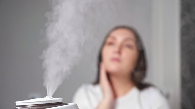 Woman in background with facial steamer blowing steam in foreground