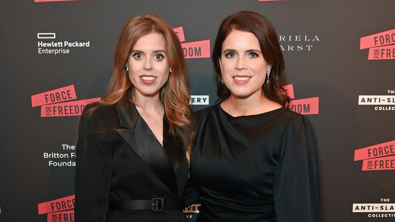 Princesses Beatrice and Eugenie of York smile while standing next to each other in black dresses