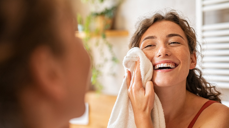 A smiling woman patting her face with a towel 