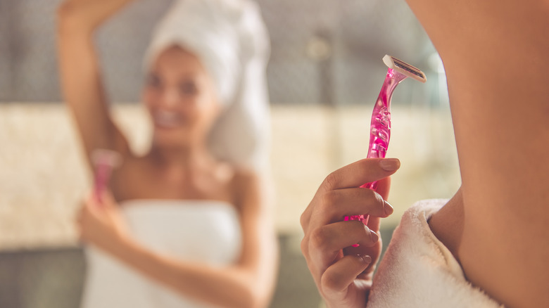 Woman shaving her underarms with a pink razor 