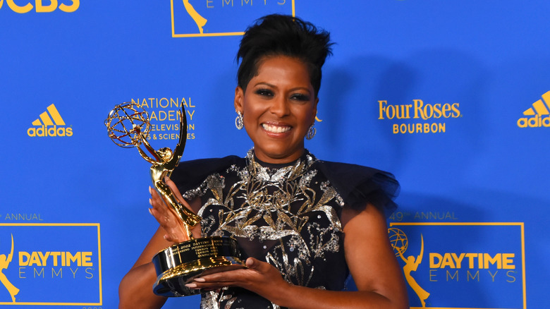 Tamro Hall smiles holding an Emmy award