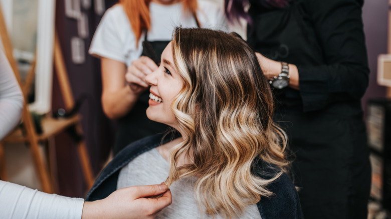 woman sits in chair at beauty salon, smiles