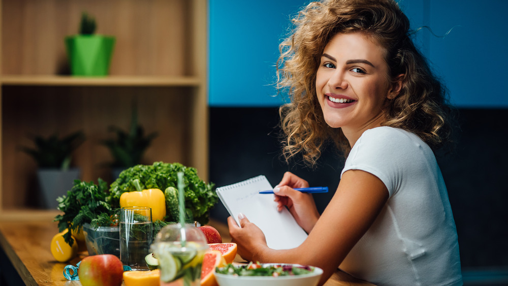 Woman smiling sitting beside vegetables and writing a list