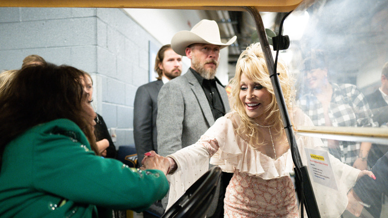 Loretta Lynn in green holds Dolly parton's hand