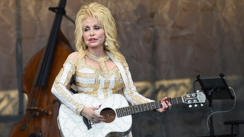 Dolly Parton performs on stage holding a guitar