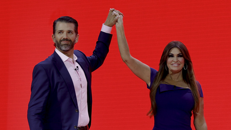 Donald Trump Jr. and Kimberly Guilfoyle holding their clasped hands in the air on stage